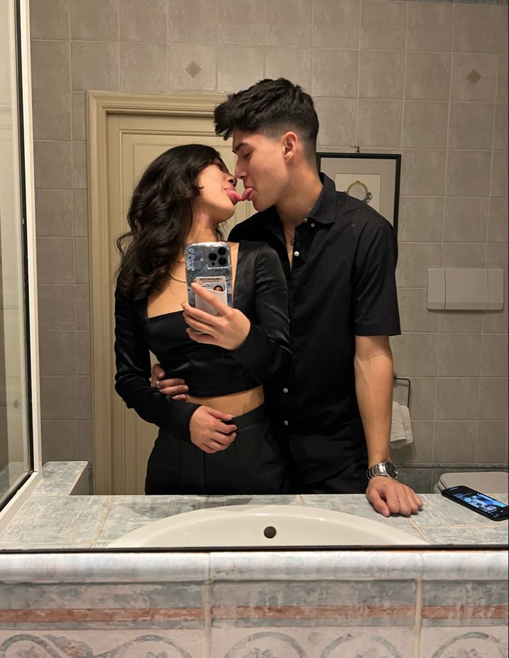 a man and woman kissing while taking a selfie in front of a bathroom mirror