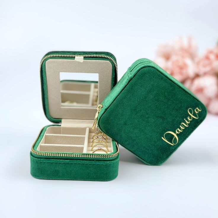 an open green velvet jewelry box sitting on top of a white table next to pink flowers