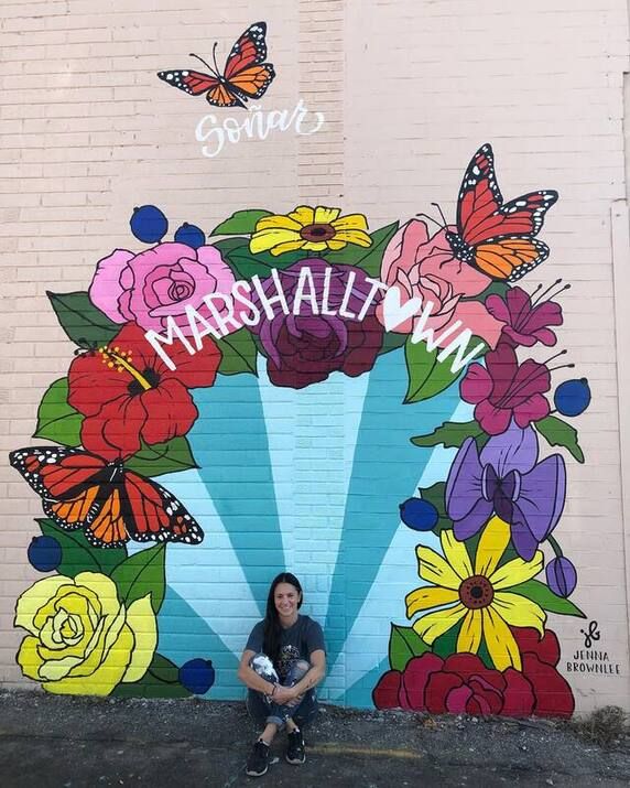 a woman sitting in front of a wall with flowers and butterflies painted on it