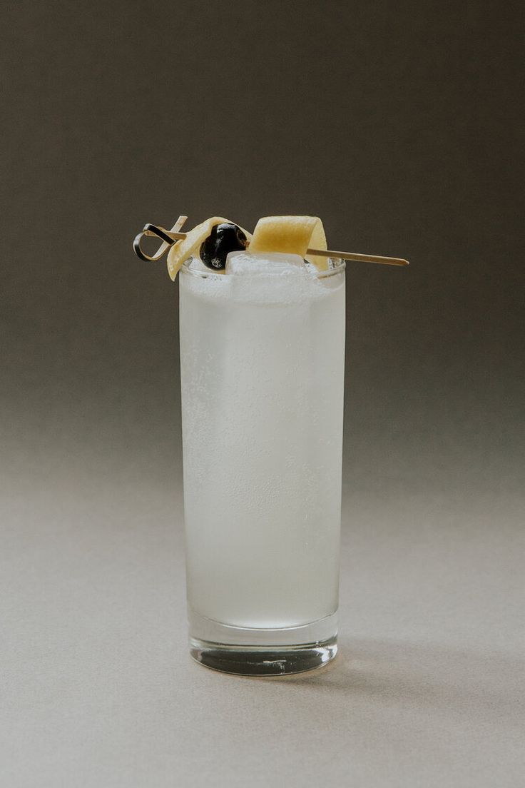 a tall glass filled with ice and topped with a lemon peel garnished with olives