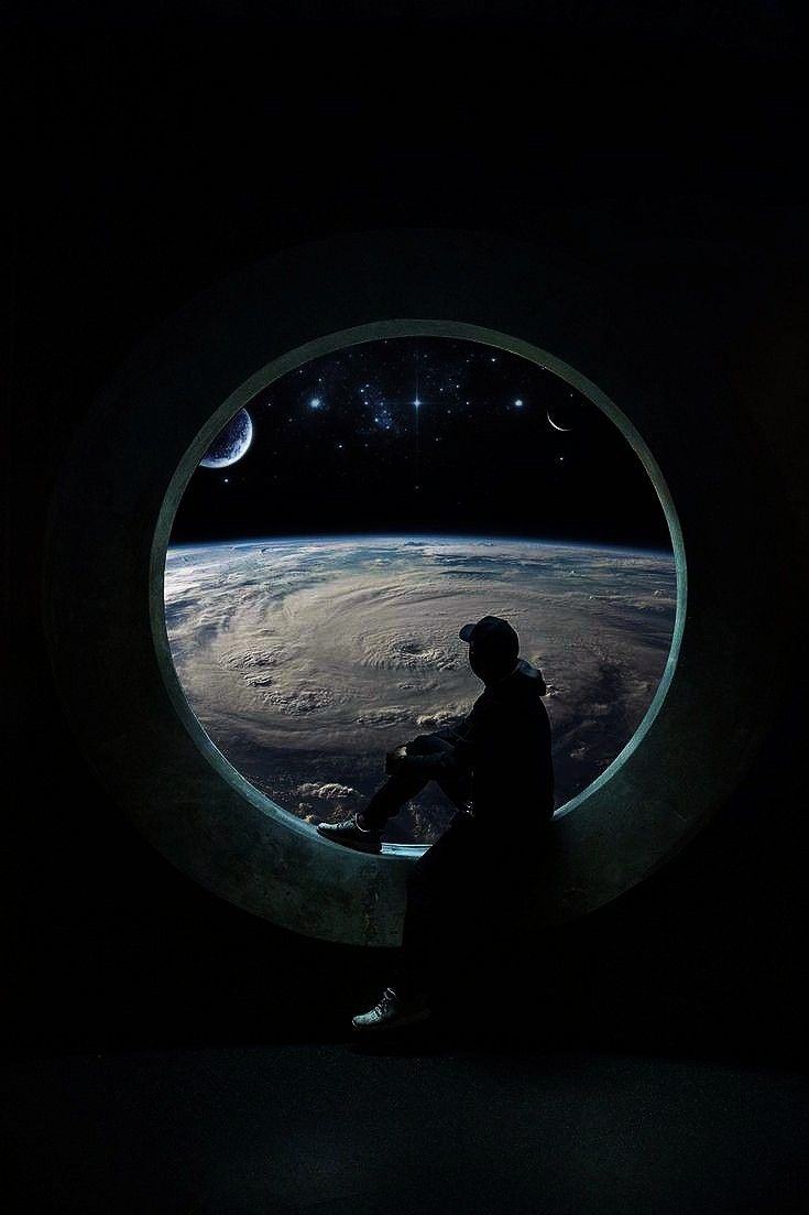 a man sitting in front of a window looking out at the earth and stars above