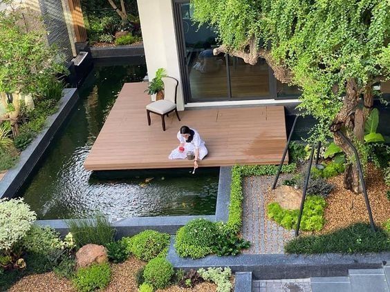 a person sitting on top of a wooden deck next to a small pond in front of a house