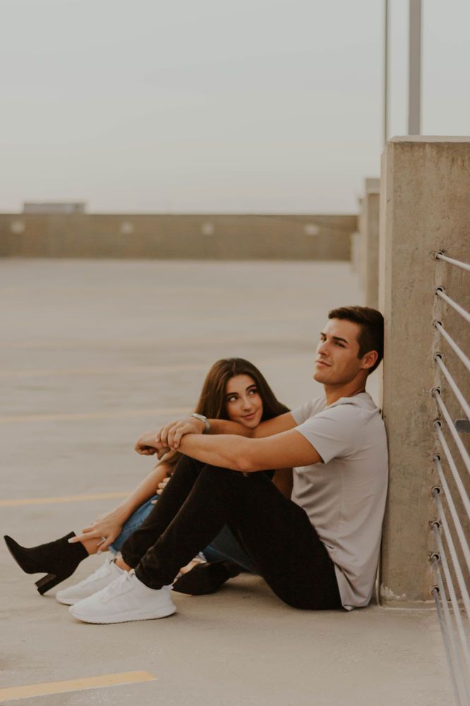 a man and woman sitting next to each other on the ground in an empty parking lot