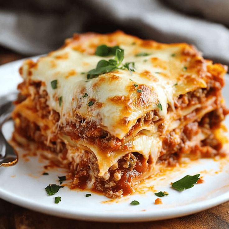 a white plate topped with lasagna covered in sauce and cheese next to a fork