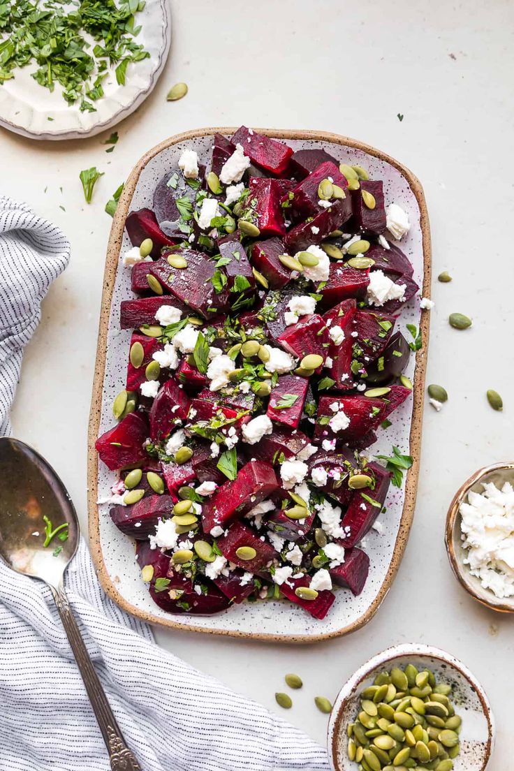 beet salad with goat cheese and pistachios on a platter next to two bowls