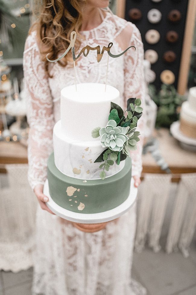 a woman holding a three tiered cake with succulents on the top