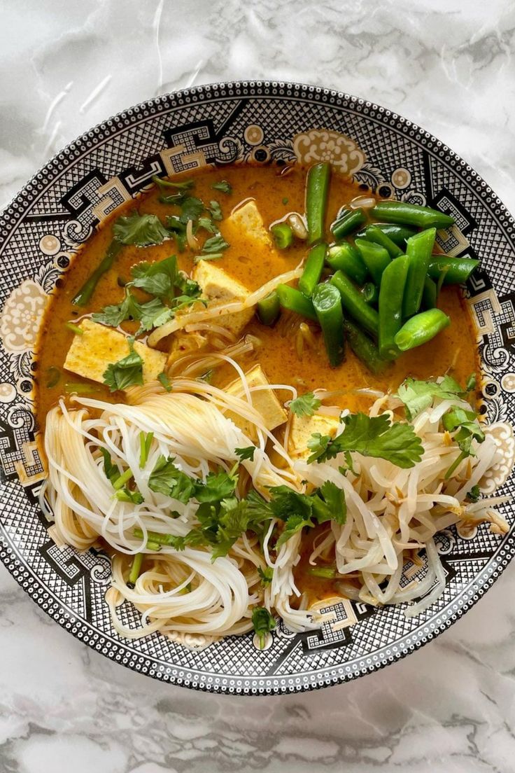 a bowl filled with noodles and vegetables on top of a marble countertop next to a spoon