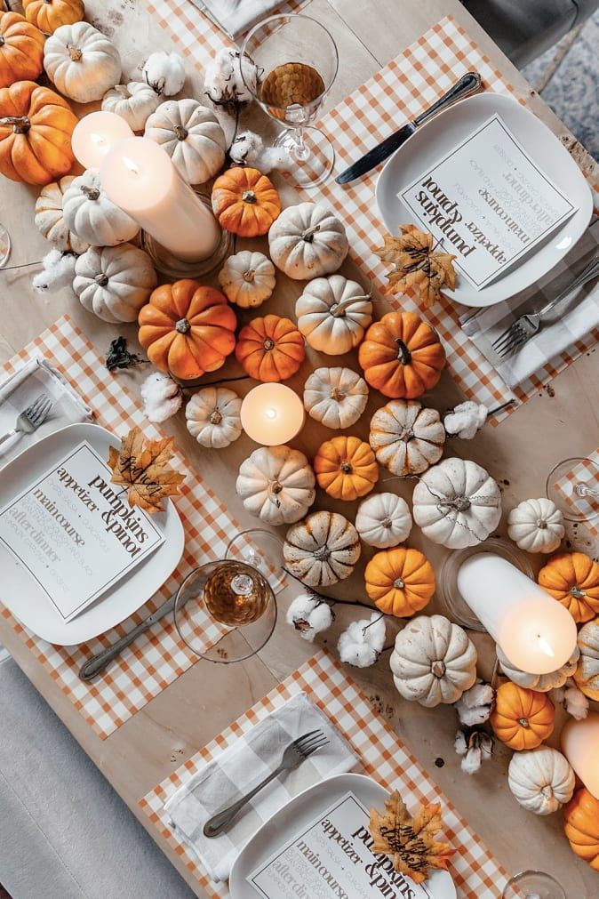 the table is set with pumpkins, candles and place settings for an autumn dinner