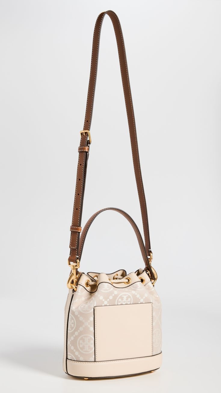 Find TORY BURCH T Monogram Bucket Bag on Editorialist. This Tory Burch bucket bag features a structured silhouette with gold-tone hardware. The bag is crafted from jacquard with a monogram pattern and leather trim. It has a drawstring top, patch interior pocket, and an optional adjustable strap. The bag is lined in suede and has a height of 8.25 inches, a length of 8.25 inches, and a depth of 4.75 inches. The strap drop is 21.75 inches and the handle drop is 4 inches. Luxury Beige Pouch Bucket Bag, Luxury Cream Bucket Bag In Pouch Shape, Luxury Cream Pouch Bucket Bag, Designer Beige Shoulder Bag With Brass Hardware, Monogram Canvas Pouch Shoulder Bag With Gold-tone Hardware, Designer Cream Bucket Bag With Detachable Handle, Luxury Cream Crossbody Bucket Bag, Luxury Cream Bucket Bag With Removable Pouch, Gold Monogram Canvas Bag With Gold-tone Hardware