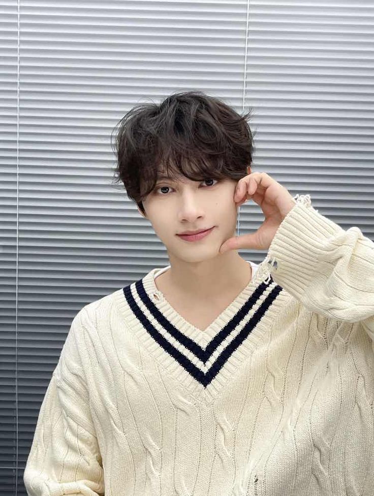 a young man wearing a white sweater posing for the camera with his hand on his head