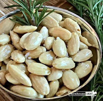 a bowl filled with almonds sitting on top of a wooden table next to rosemary sprigs