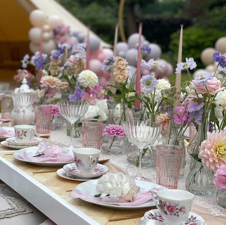 a long table is set with pink and white plates, cups, and saucers