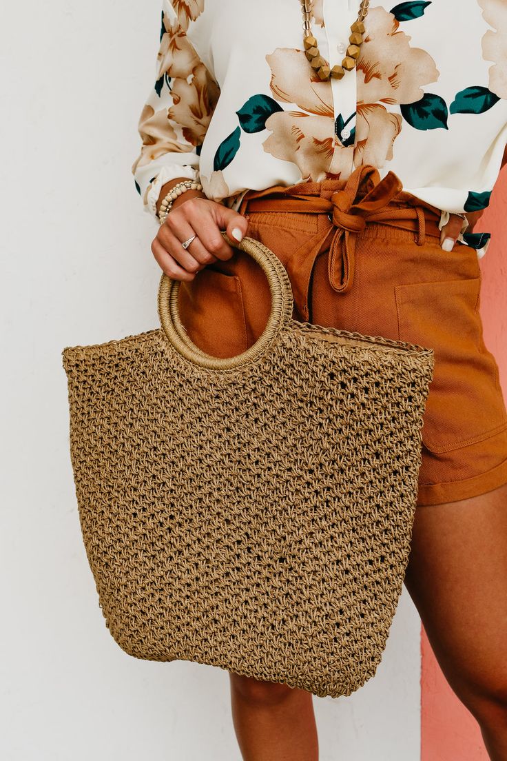 a woman is holding a straw bag in her right hand and wearing brown shorts with an off - white blouse