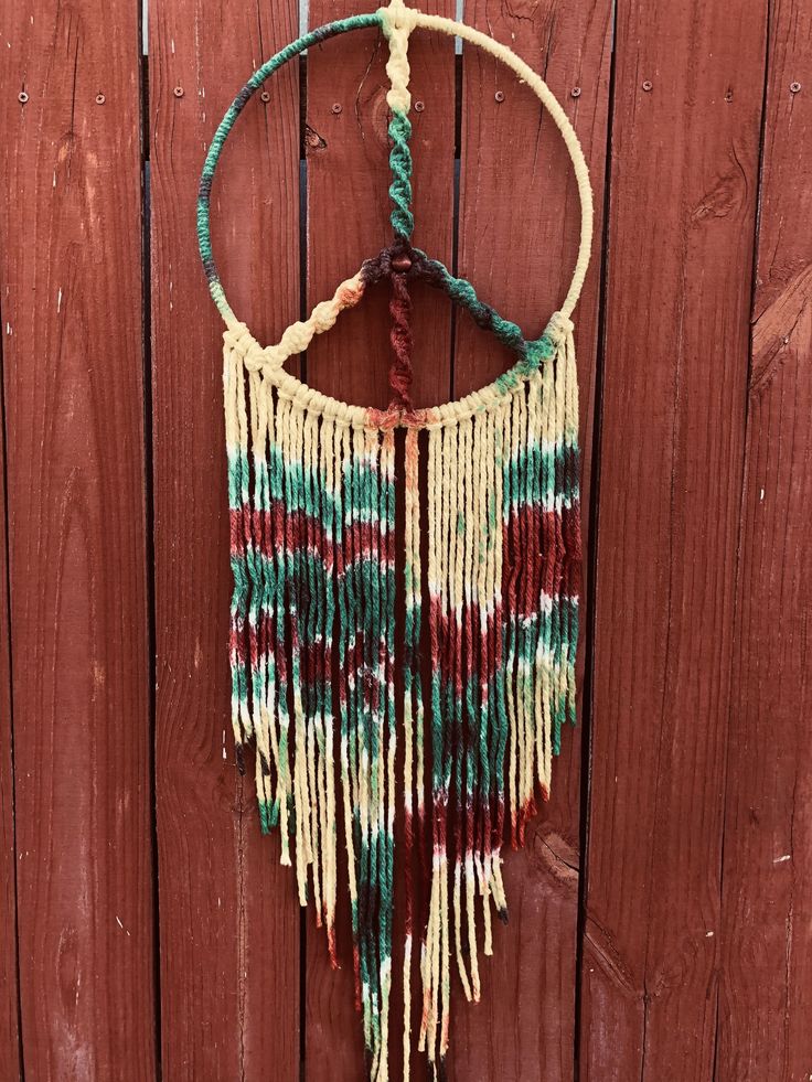 a small macrame hanging on a wooden wall next to a brown and white fence