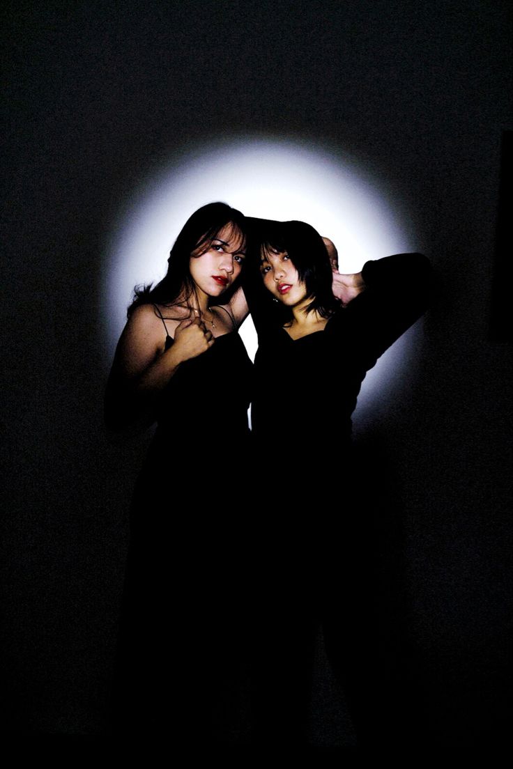 two women standing in the dark with their arms around each other and one holding her head