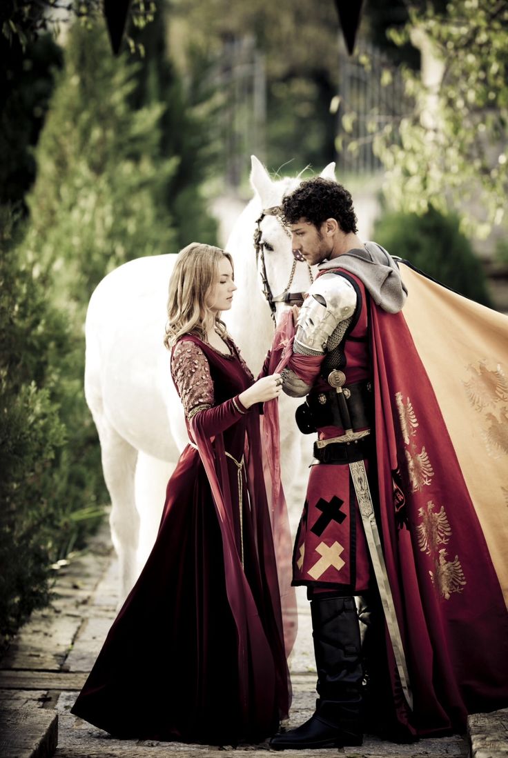 a man and woman dressed in medieval clothing standing next to a white horse