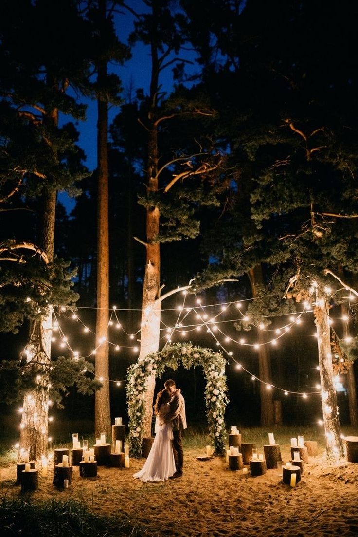 a bride and groom standing in the middle of a forest at night with fairy lights