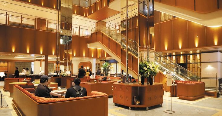 two men sitting on couches in a lobby with stairs and glass railings to the second floor