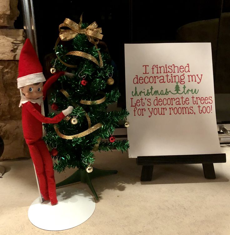 an elf standing next to a christmas tree with a sign in front of it that says i finished decorating my christmas tree let's decorate trees for your roots, too