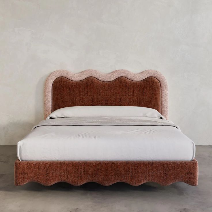 an upholstered bed with scalloped headboard and foot board, against a white wall