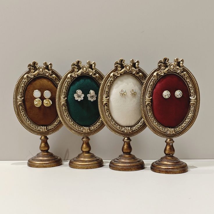 three different colored frames with pearls on them sitting in front of a white wall and two gold pedestals