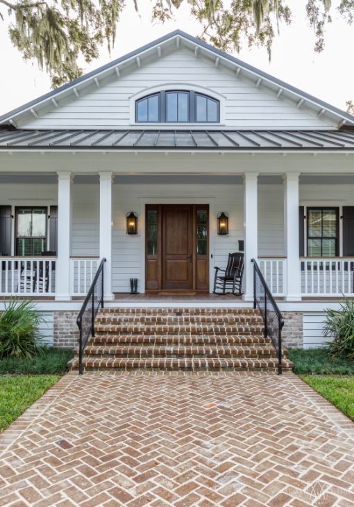 a white house with brick steps leading to the front door and porch area, surrounded by greenery