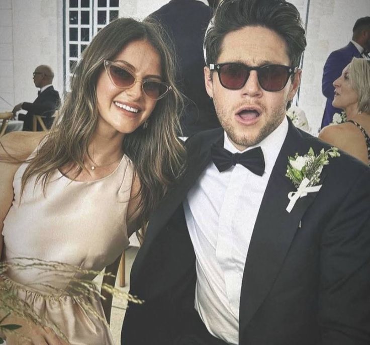 a man in a tuxedo standing next to a woman wearing sunglasses and a dress