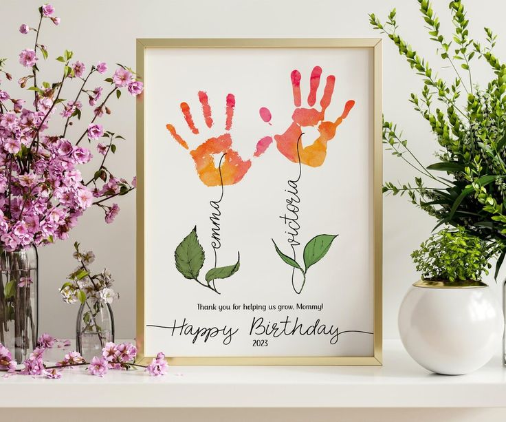 two handprints are displayed on a shelf next to flowers