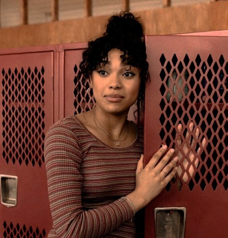 a woman standing in front of lockers holding her hands on the door and looking at the camera