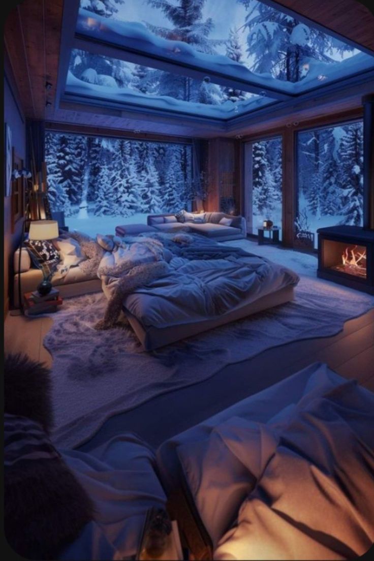 a bedroom with snow covered trees in the background and a fireplace lit up at night