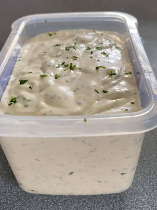 a plastic container filled with white sauce and garnished with green sprigs