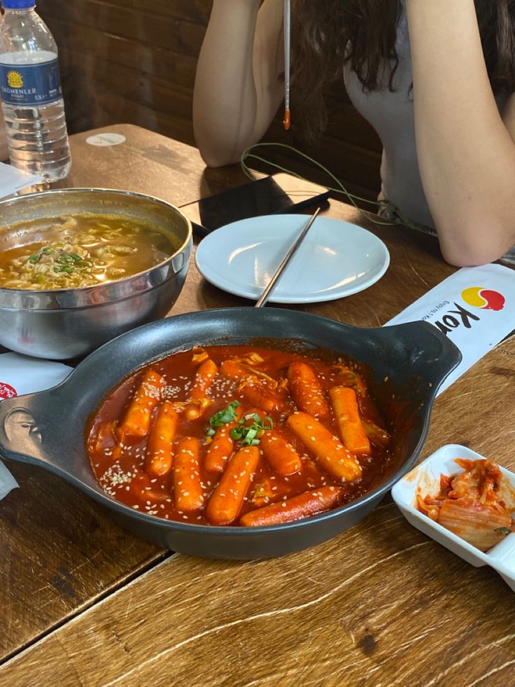 a woman sitting at a table with some food in a pan on the table next to her