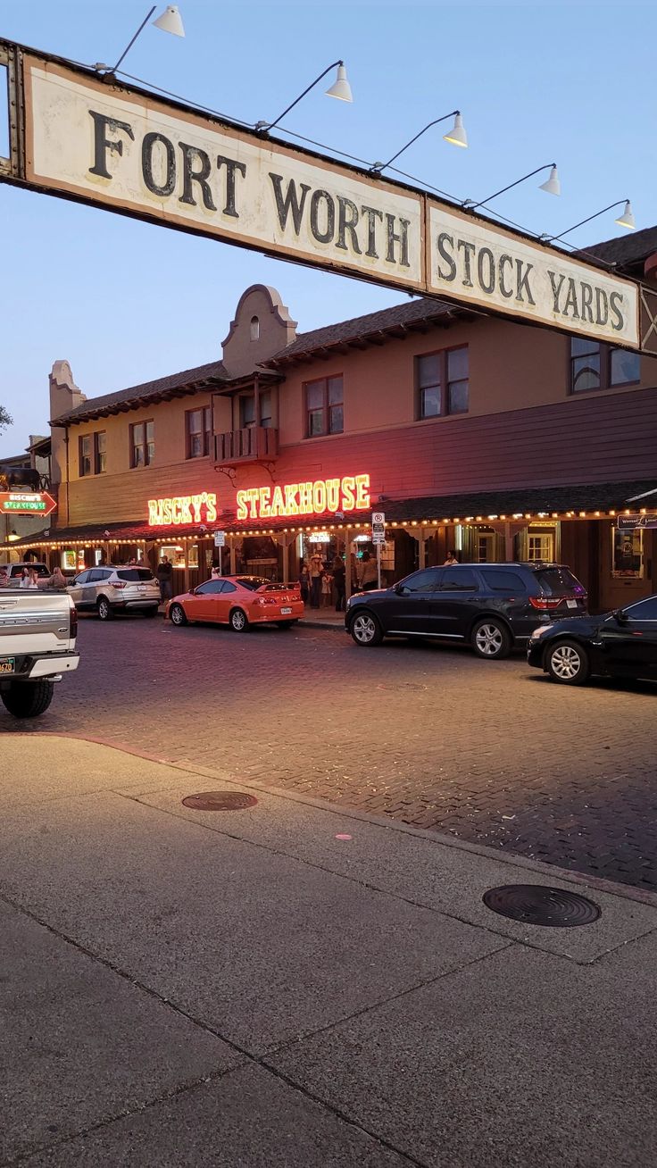 cars are parked on the street in front of a building with a sign that says fort worth stock yards