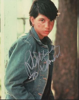 an autographed photo of a young person wearing a jean jacket and jeans, with trees in the background