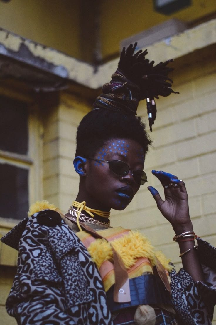 a woman with blue makeup and feathers on her head standing in front of a building