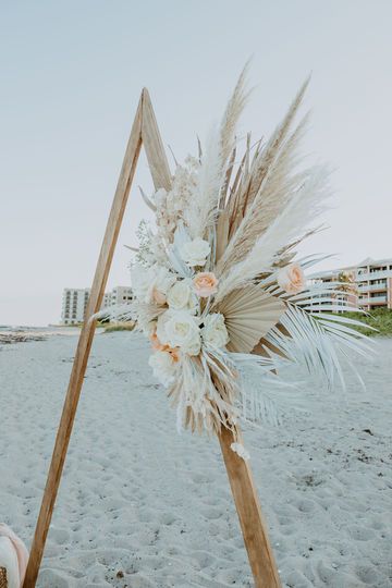 a wedding ceremony setup on the beach with pamodia and white flowers in an easel