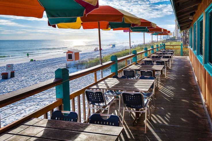 tables and chairs are lined up under umbrellas on the deck overlooking the beach at sunset