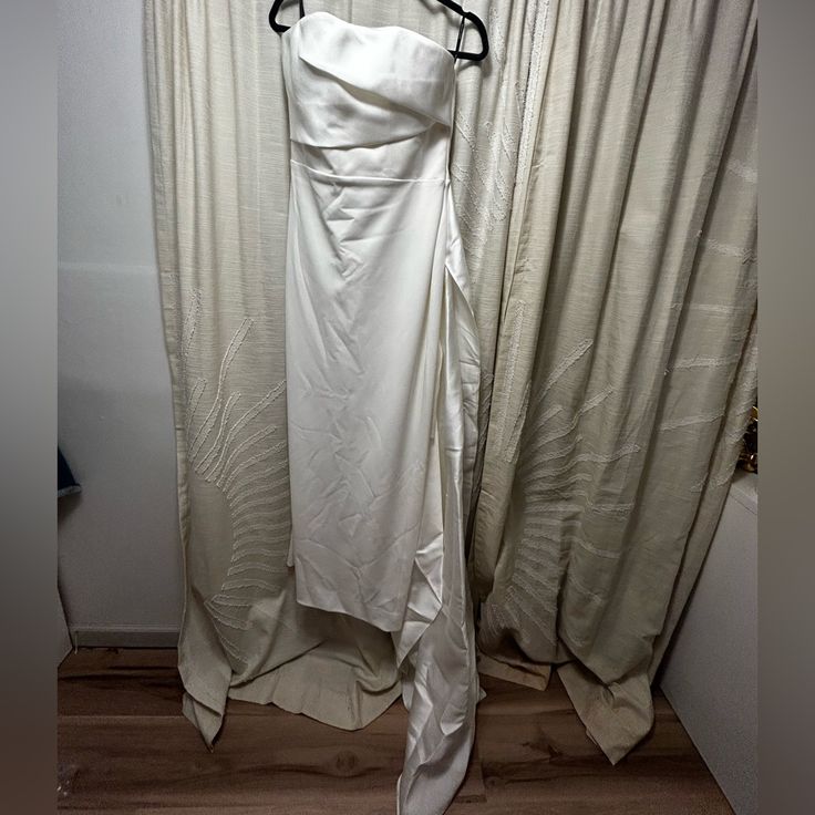 a white dress hanging on a hanger in front of curtains