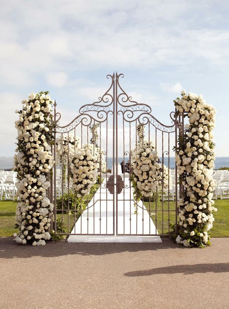 an iron gate decorated with white flowers and greenery for a wedding ceremony at the beach