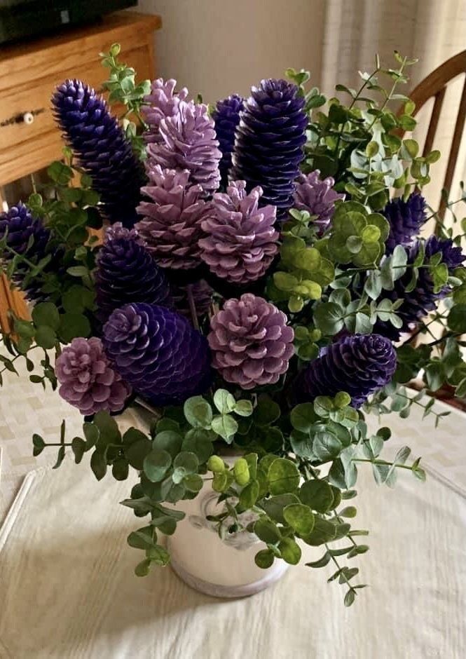 purple and green flowers in a white vase on a dining room table with greenery