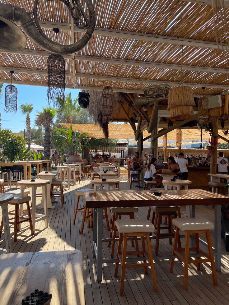 an outdoor restaurant with tables and chairs under a straw roof over looking the ocean or beach