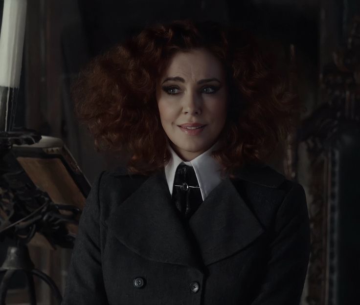 a woman with red hair wearing a coat and tie in a dark room next to a bicycle