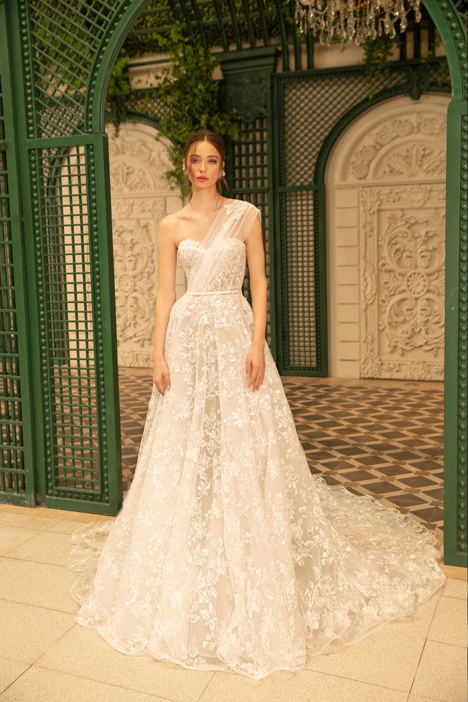 a woman standing in front of a green archway wearing a white dress with flowers on it