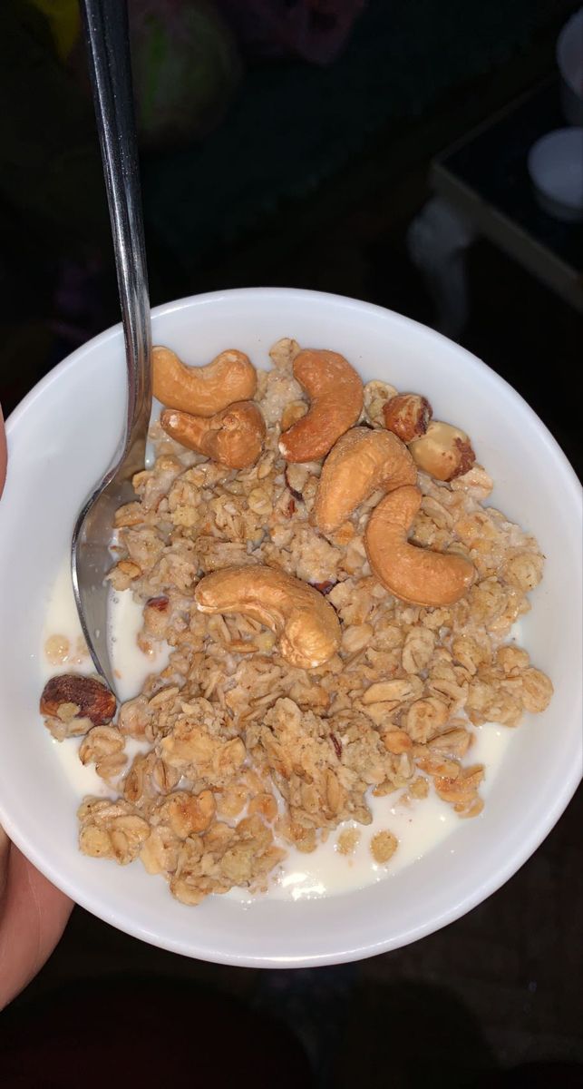 a person holding a bowl of cereal with a spoon in it and some nuts on top