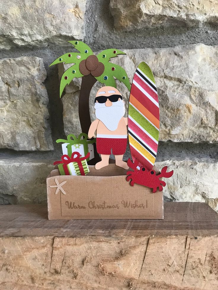 a cardboard cutout of a santa clause holding a surfboard and christmas presents in front of a stone wall