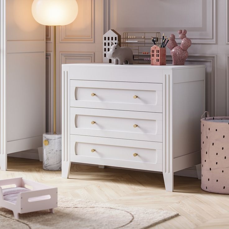 a white chest of drawers in the corner of a room with pink accessories on it