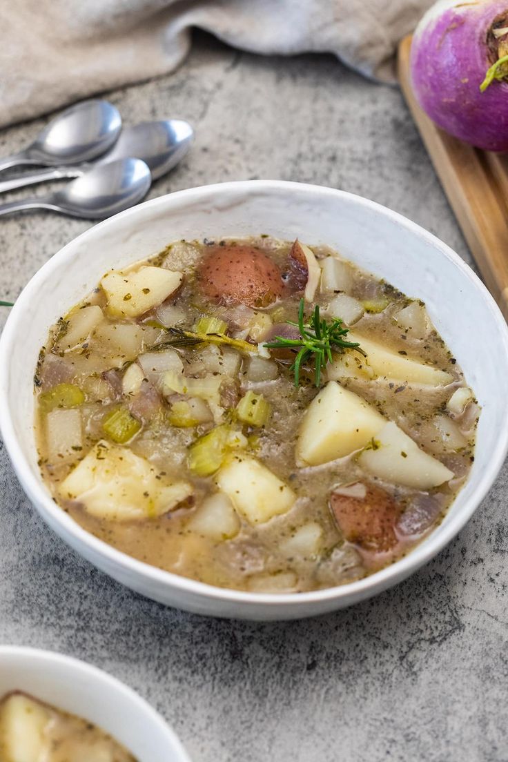 two bowls of soup with potatoes and carrots next to some spoons on a table