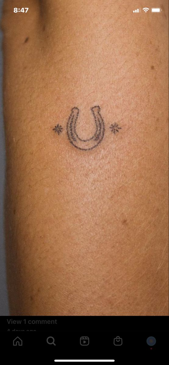 a small horseshoe tattoo on the back of a woman's arm, with an arrow in the middle