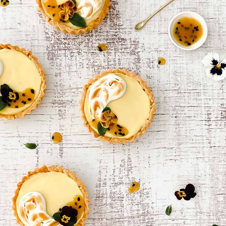 four small pies with cream filling and flowers on the side, sitting on a white surface