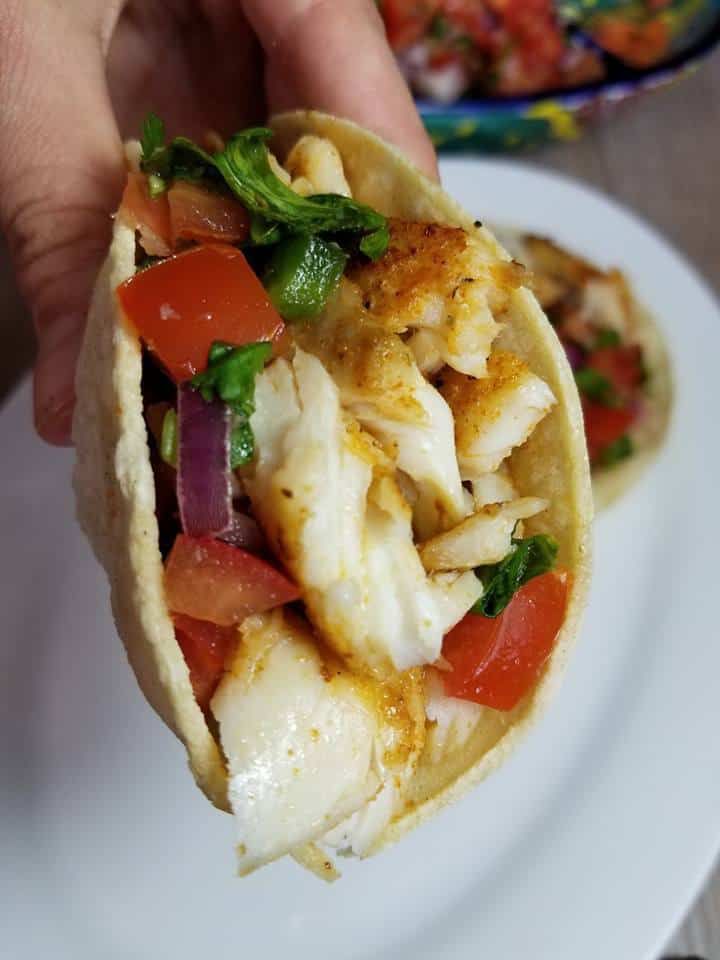 a hand holding a taco filled with meat and veggies on top of a white plate